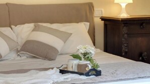 Uma cama bem arrumada com travesseiros listrados, uma mesa de cabeceira com abajur e um pequeno vaso com flores.