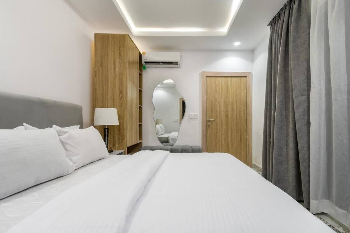 Una habitación de hotel moderna con una cama grande, una lámpara de noche, un armario, un espejo y un equipo de aire acondicionado.