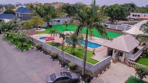 A residential area with a swimming pool, palm trees, and a car parked on the street. - De Castle hotels & Resort (Enugu)