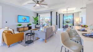 A modern living room with a sofa, armchairs, a dining area with a long table, and a TV mounted on the wall. - Sleeps 8 - Heated Pool - Games - Quiet area - Stars Vacation Rentals (Cape Coral)