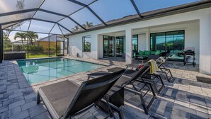 A modern outdoor pool area with a glass enclosure, lounge chairs, and a patio with outdoor furniture. - Sleeps 8 - Heated Pool - Games - Quiet area - Stars Vacation Rentals (Cape Coral)