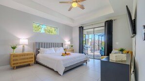 A modern bedroom with a large bed, two bedside tables, a ceiling fan, and a sliding glass door leading to an outdoor area. - Sleeps 8 - Heated Pool - Games - Quiet area - Stars Vacation Rentals (Cape Coral)