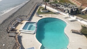 Una piscina dalle linee curve, circondata da una terrazza con lettini e una piccola area giardino.