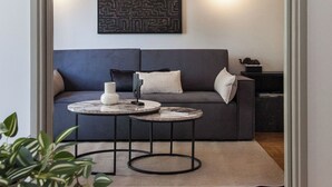 A modern living room with a grey sofa, a round coffee table, and a patterned wall hanging. - Fashionable Apt in Ano Kipseli w Balcony (Athens)