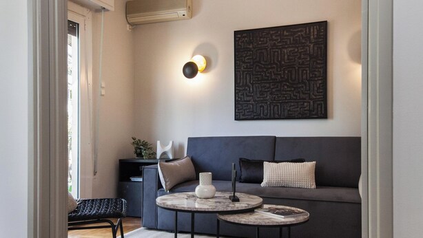 A modern living room with a grey sofa, round coffee table, and a chandelier with multiple lights. - Fashionable Apt in Ano Kipseli w Balcony (Athens)