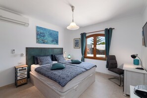 Ein Schlafzimmer mit Bett, Nachttisch, Lampe, Stuhl und einem Fenster mit Vorhängen.