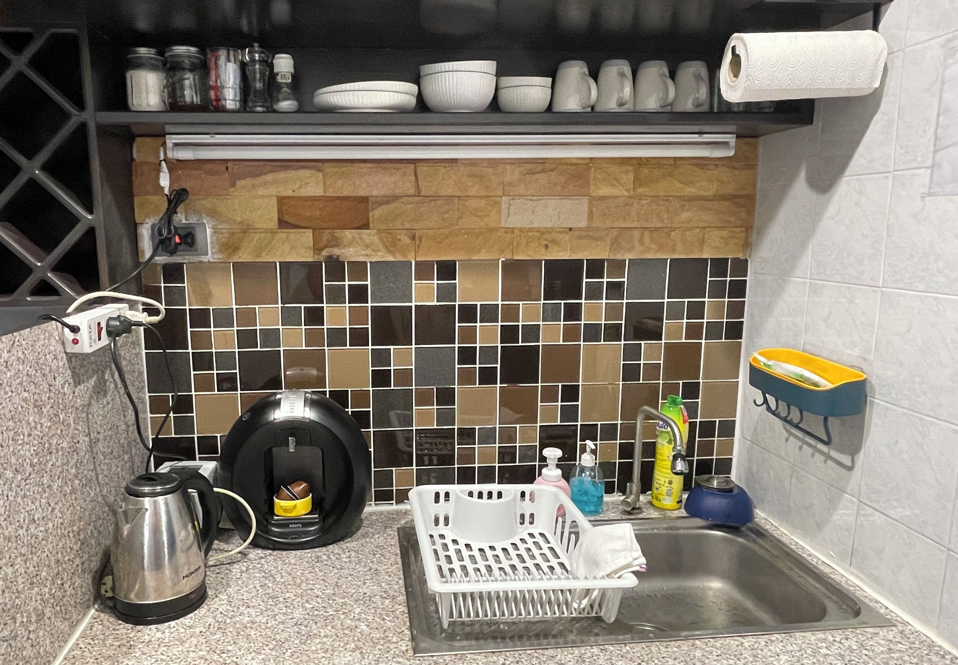 Cozinha com painel de azulejos, cafeteira, chaleira, escorredor de louça e pia.