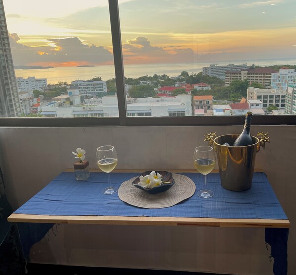 A table with a bottle of champagne, two glasses, a bowl of flowers, and a small vase on a blue tablecloth.