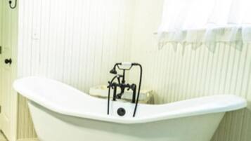 Une salle de bain avec une baignoire sur pieds, un lustre, une fenêtre avec un rideau blanc et un sol carrelé.