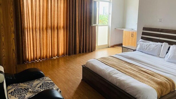 A hotel room with a large bed, a wooden wardrobe, a small table, and a view of the outdoors through a window. - Goza Guest House (Addis Ababa)