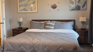 Quarto com uma cama grande, duas mesas de cabeceira, um ventilador de teto e duas pinturas penduradas na parede.