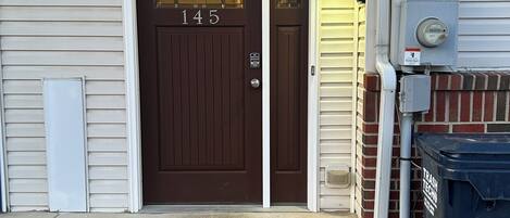 A brown double door with the number 145, a black doormat, and a trash can labeled "TRASH TECH" on the right.