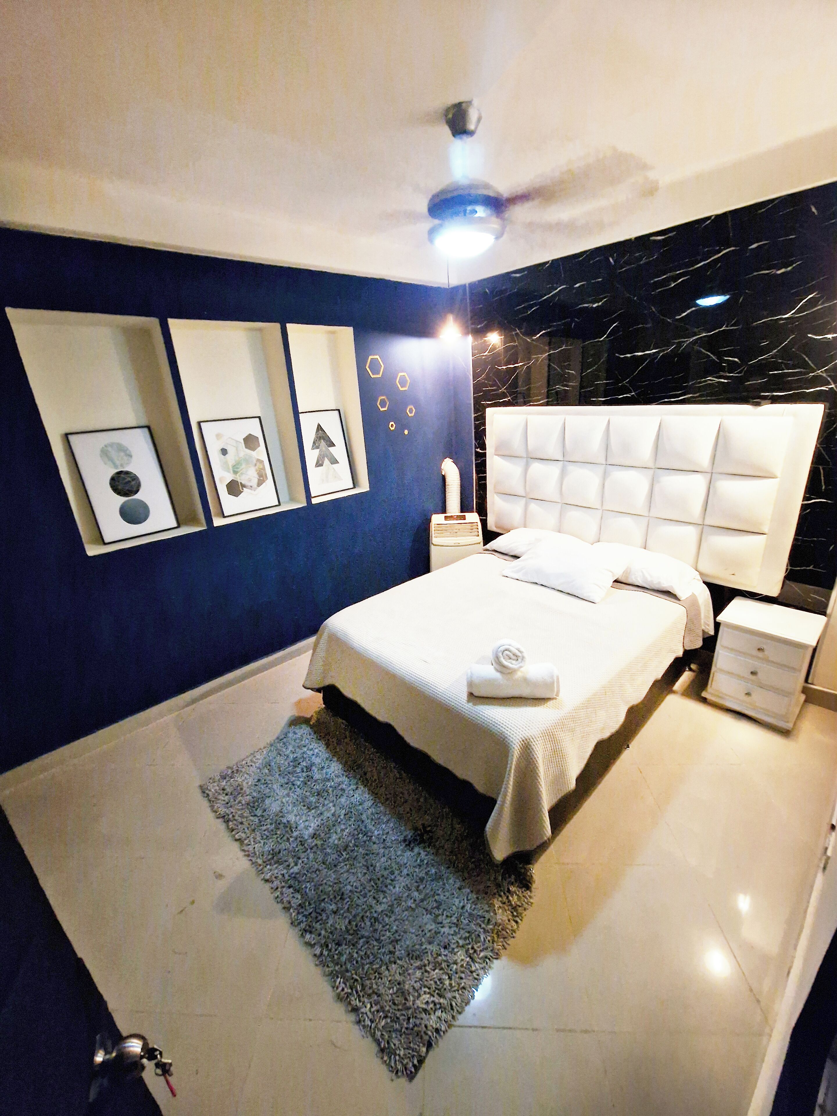 Un dormitorio moderno con una cama grande, cabecera blanca y ventilador de techo.