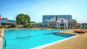 Une piscine à l’eau d’un bleu cristallin, entourée de chaises longues et de parasols, avec un bâtiment visible au loin.