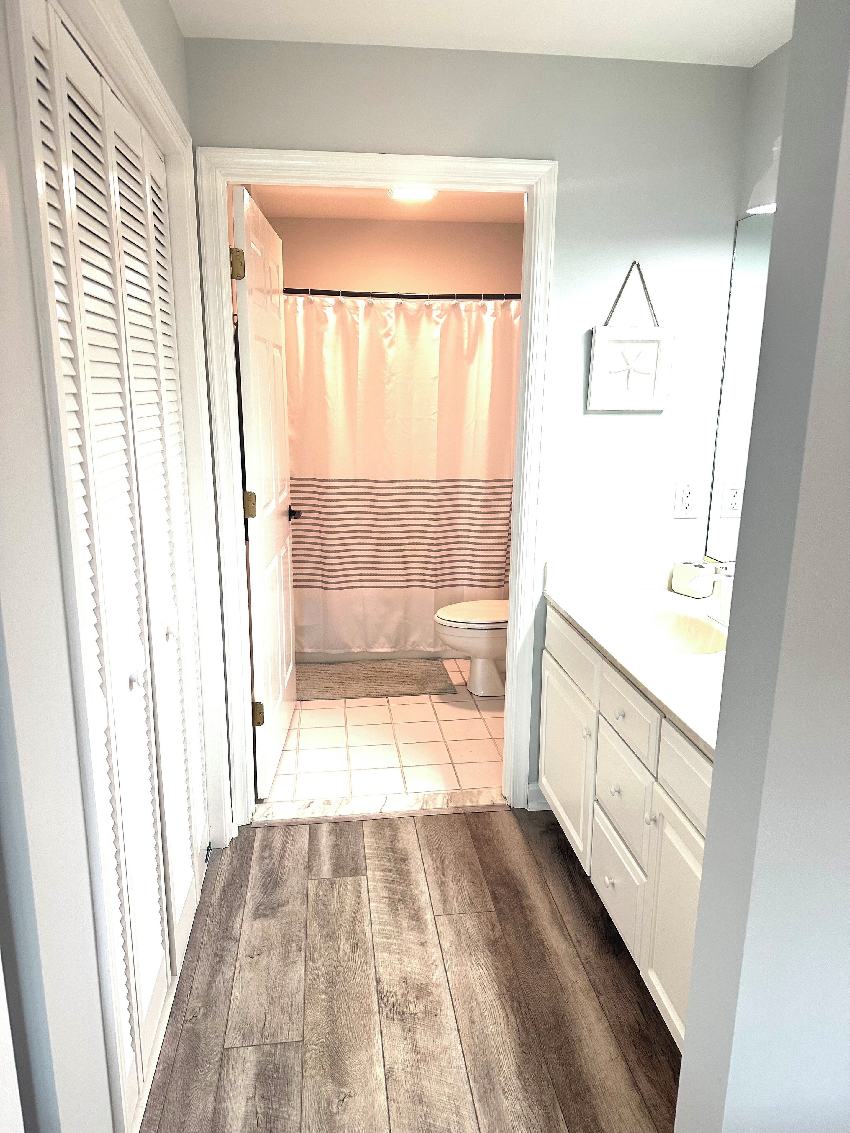 Un pasillo estrecho con piso de madera que conduce a un baño con cortina de ducha a rayas y un inodoro.