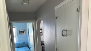 A hallway with wooden flooring, a bed with blue bedding, and a white wardrobe with two doors.