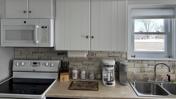 A kitchen with white cabinets, a microwave, a stove, a coffee maker, and a sink.