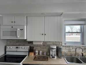 A kitchen with white cabinets, a microwave, a stove, a coffee maker, and a sink.