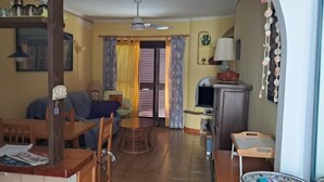 A cozy living room with a dining area, a television, and a window with curtains. - Mojacar Beach 2 Bedroom House With sea View (Mojacar)