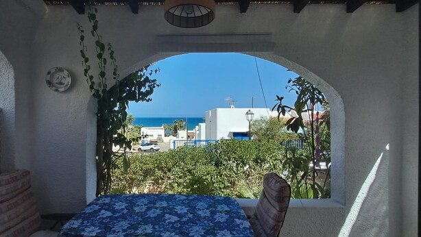 A balcony with a table and chairs, a view of the sea, and a building in the background. - Mojacar Beach 2 Bedroom House With sea View (Mojacar)