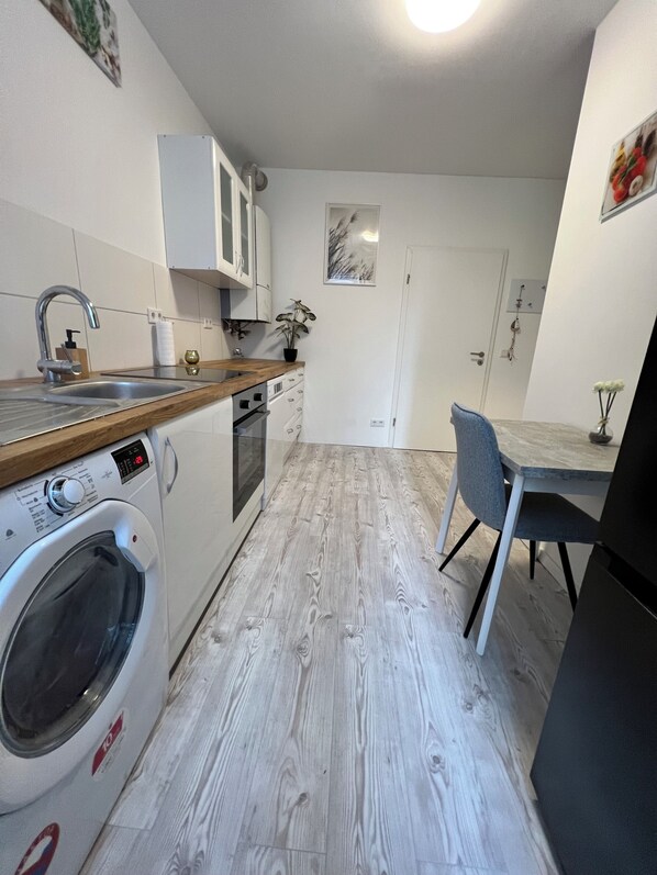 Une cuisine compacte dotée d’un lave-linge intégré, d’un plan de travail en bois et d’un coin repas avec une table et une chaise.