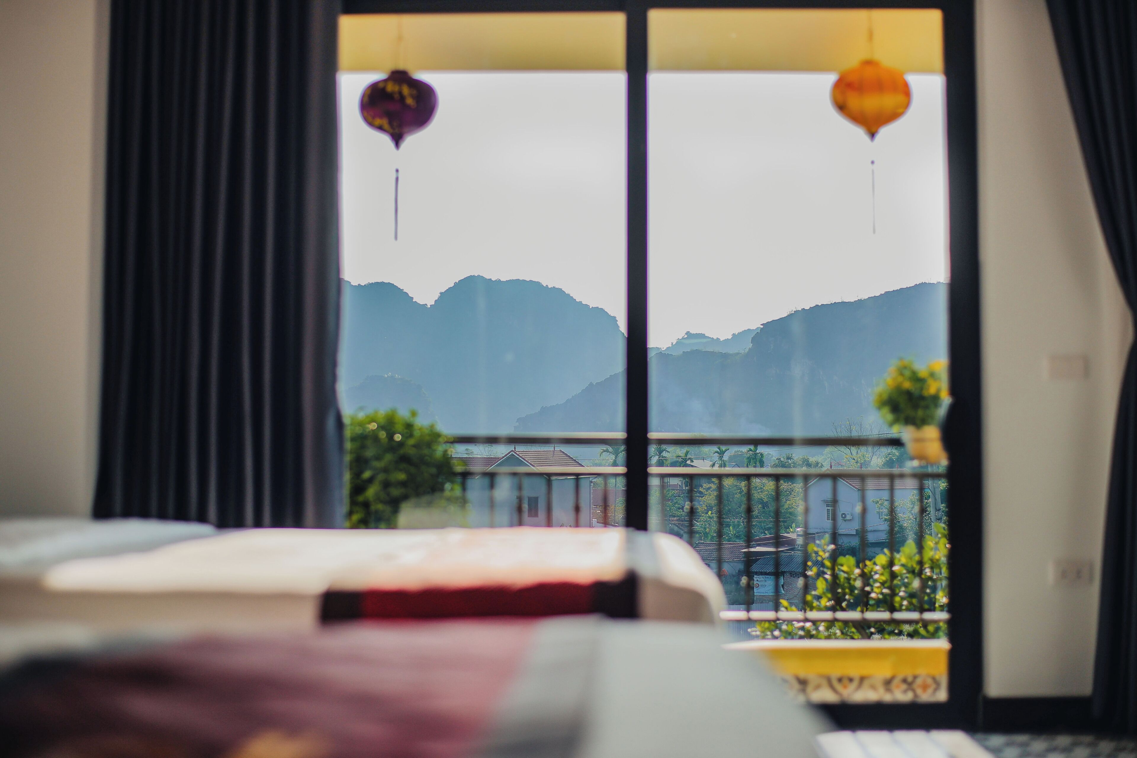 Ein Hotelzimmer mit Bett, Blick auf Berge durch große Fenster und einem Balkon mit Pflanzen.