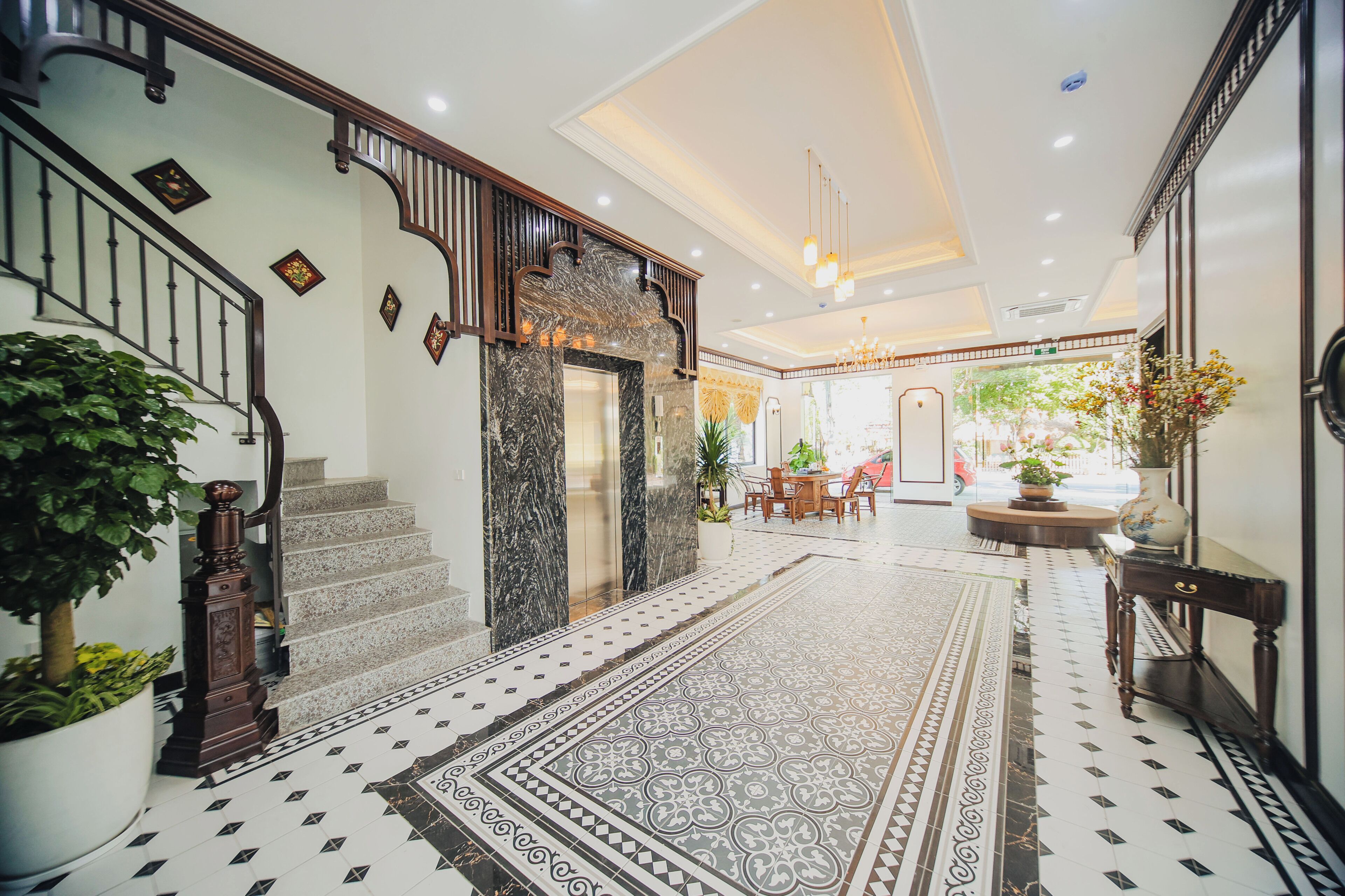 A spacious lobby with a grand staircase, a patterned floor, and a dining area with a view of the outdoors.