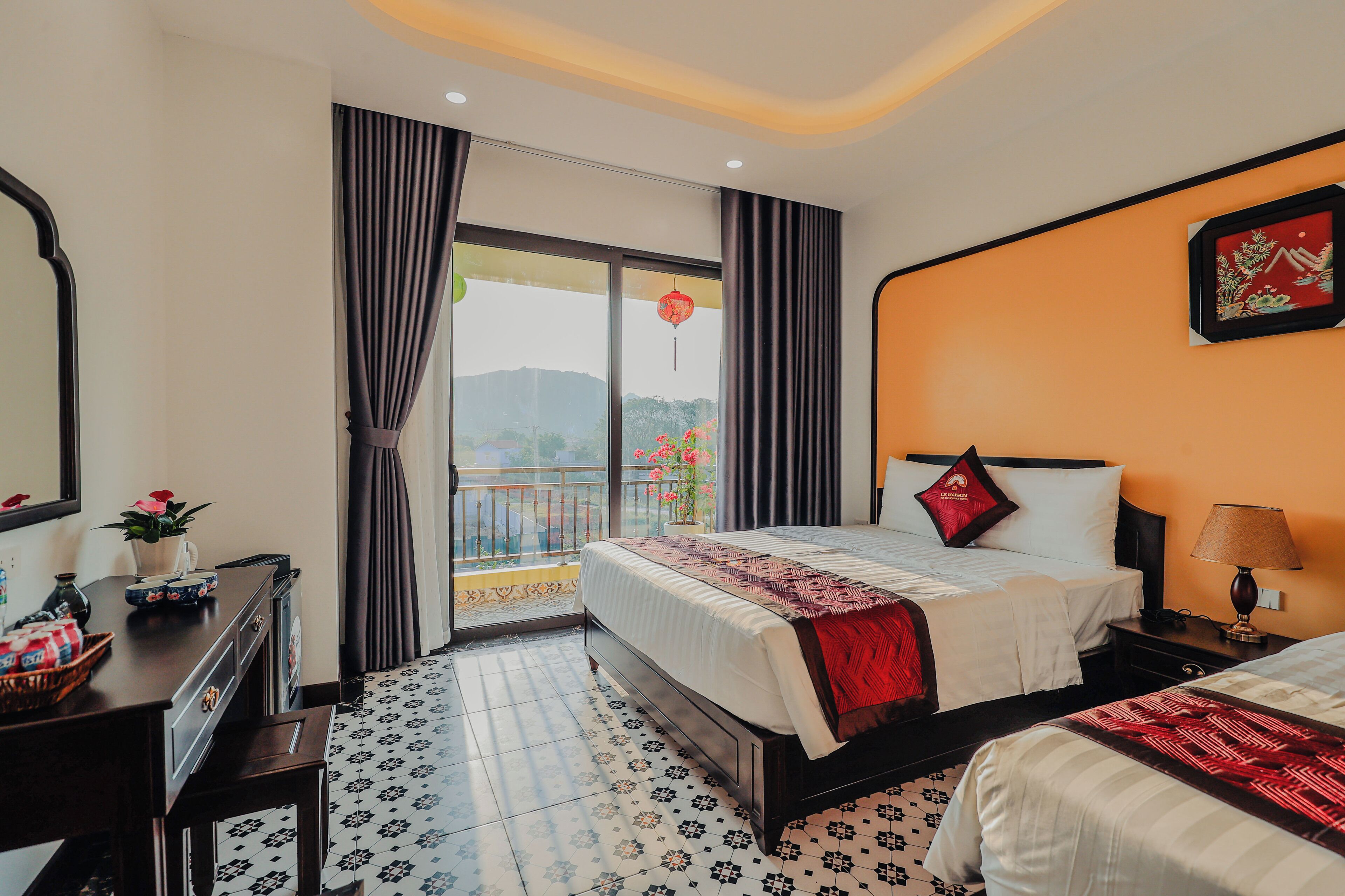 A hotel room with a bed, a bedside table with a lamp, a dresser, and a view of the outdoors through a window.