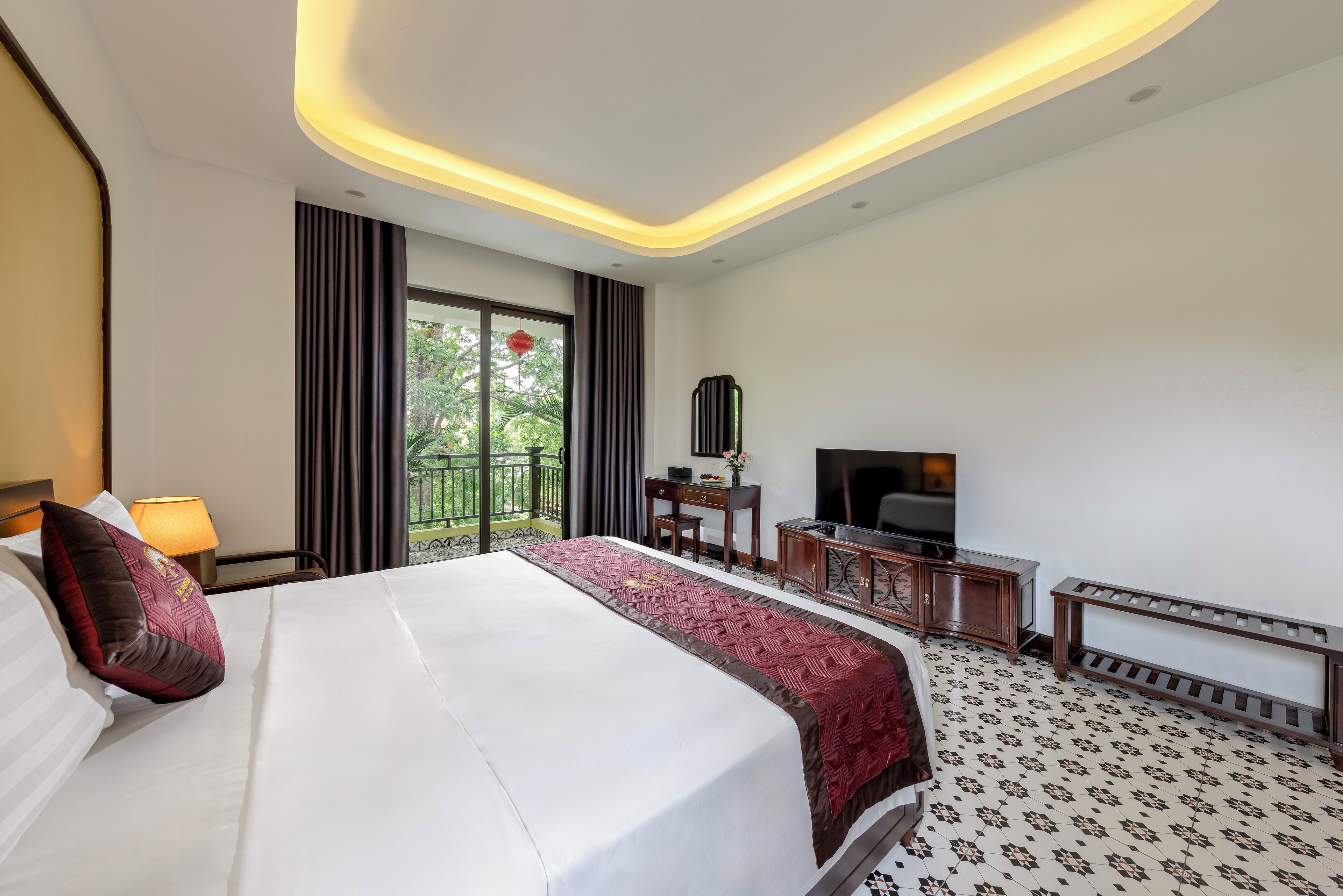 Habitación de hotel con una cama grande, escritorio, televisor y balcón con vistas a zonas verdes.