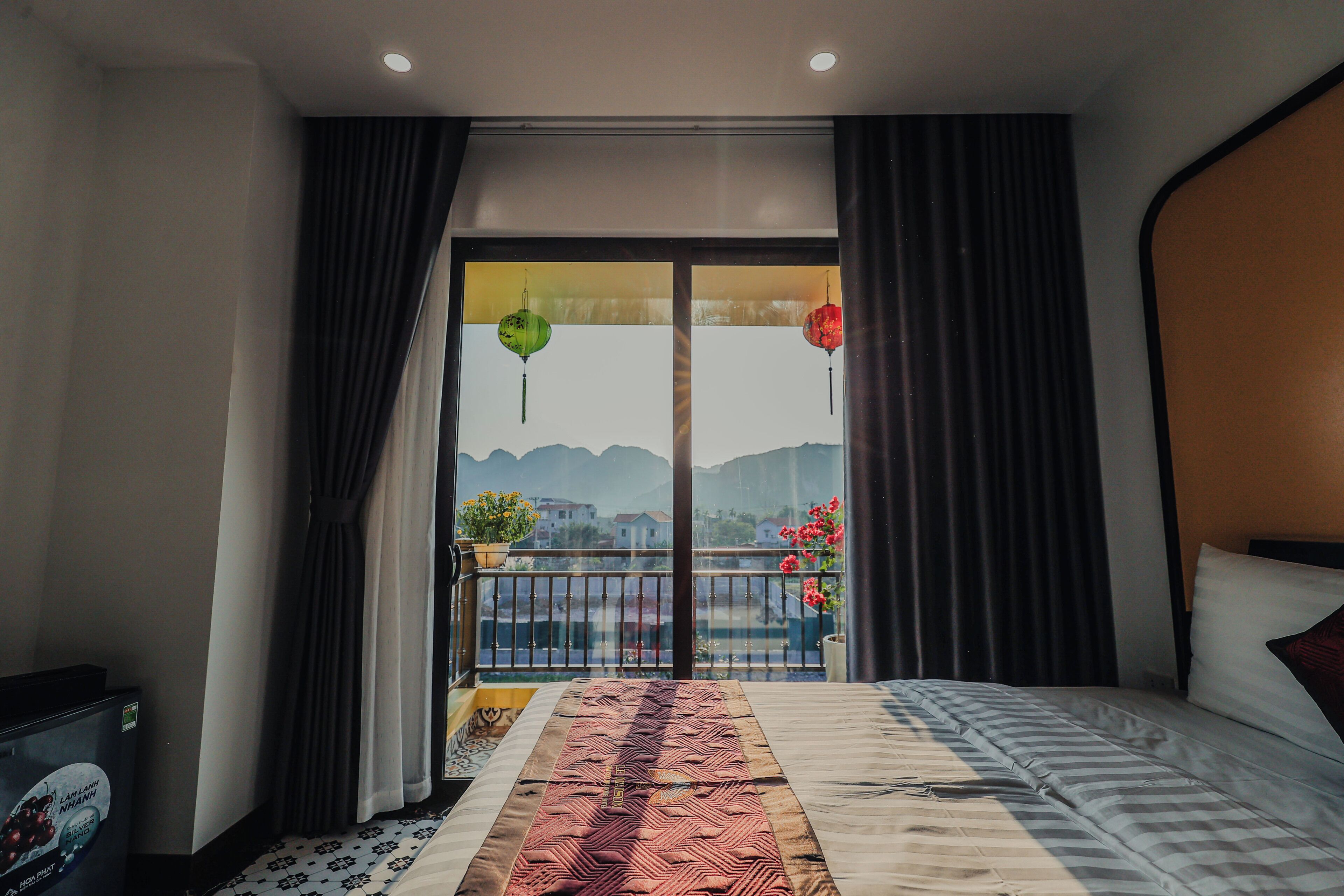 A hotel room with a bed, a balcony with a view, and a window with curtains.