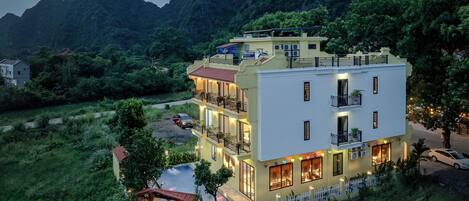 Un hôtel à plusieurs étages doté d’une piscine, entouré d’une végétation luxuriante et de montagnes.