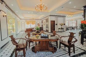 Un hall d’hôtel spacieux avec une table de salle à manger ronde entourée de chaises, un lustre et un sol à motifs.