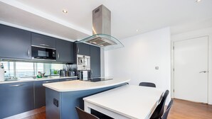 A modern kitchen with dark cabinetry, a white countertop, and a glass hood. - Cosy Corner Apartment Near to Excel (London)
