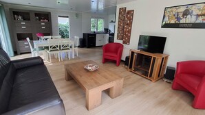 A modern living room with a black leather sofa, a wooden coffee table, and red chairs. There is a kitchen area in the background with white cabinets and a dining table.