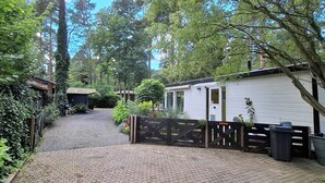 A gated pathway leading to a white mobile home with a covered porch, surrounded by lush greenery and trees.
