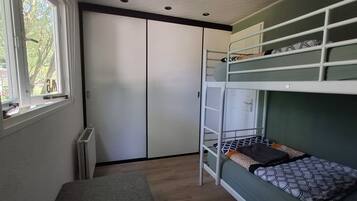 Un lit superposé avec une échelle, une fenêtre et une armoire, dans une pièce aux murs de couleur claire et dotée d’un radiateur.