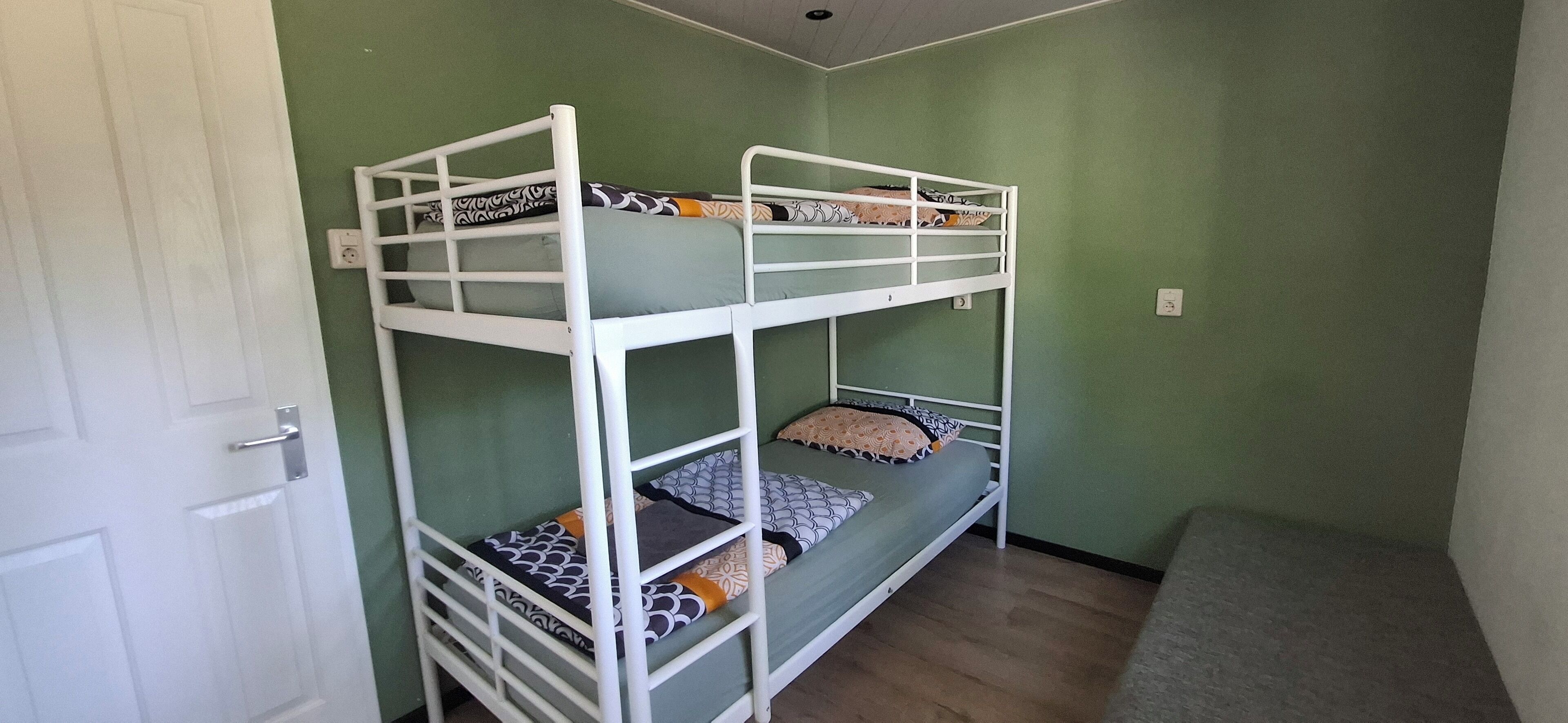 Een slaapkamer met een stapelbed, groene wanden, een witte deur en een grijze vloer.