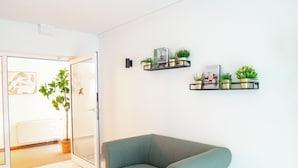 A modern living room with a green sofa, a potted plant, and two wall-mounted shelves with decorative items. - Waldhotel Schöneiche - Self-Check-in (Schoeneiche bei Berlin)