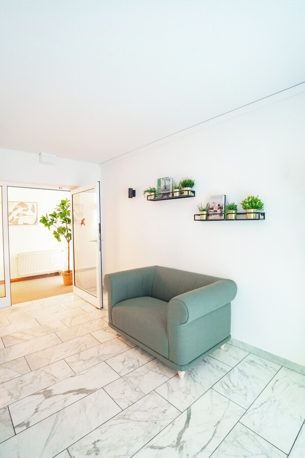 A modern living room with a green sofa, a potted plant, and two wall-mounted shelves with decorative items. - Waldhotel Schöneiche - Self-Check-in (Schoeneiche bei Berlin)