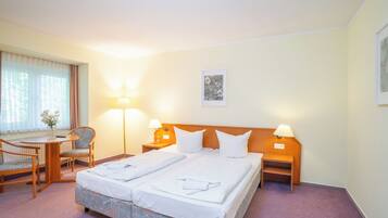 Quarto de hotel com cama de casal, duas mesas de cabeceira com luminárias, uma pequena escrivaninha com cadeira e uma janela com cortinas.