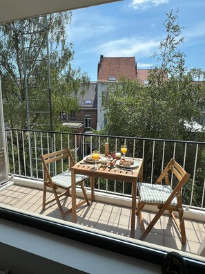 A balcony with a wooden table set for breakfast, two wooden chairs, and a railing.