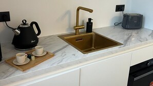 A modern kitchen with a marble countertop, a gold faucet, a kettle, a toaster, and a dishwasher.