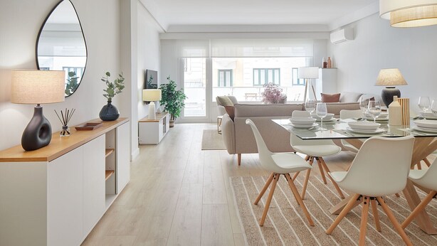 Een moderne, goed verlichte eetruimte met een glazen tafel, witte stoelen en een stadszicht door grote ramen.