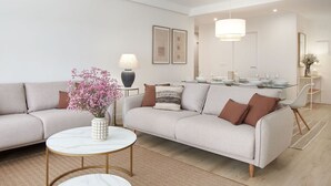 Een moderne woonkamer met een beige bank, twee ronde marmeren bijzettafels en een vaas met roze bloemen.