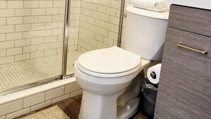 A bathroom with a glass-enclosed shower, a toilet, a sink, and a framed picture on the wall. - Cozy Studio Near Coral Gables (Miami)