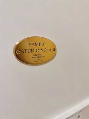 Une plaque de couleur or portant l’inscription « FAMILY STUDIO NO. 17 » et « PENSIONAT PRINSHÖJDEN, propriété d’ANDREAS et DAVID ».