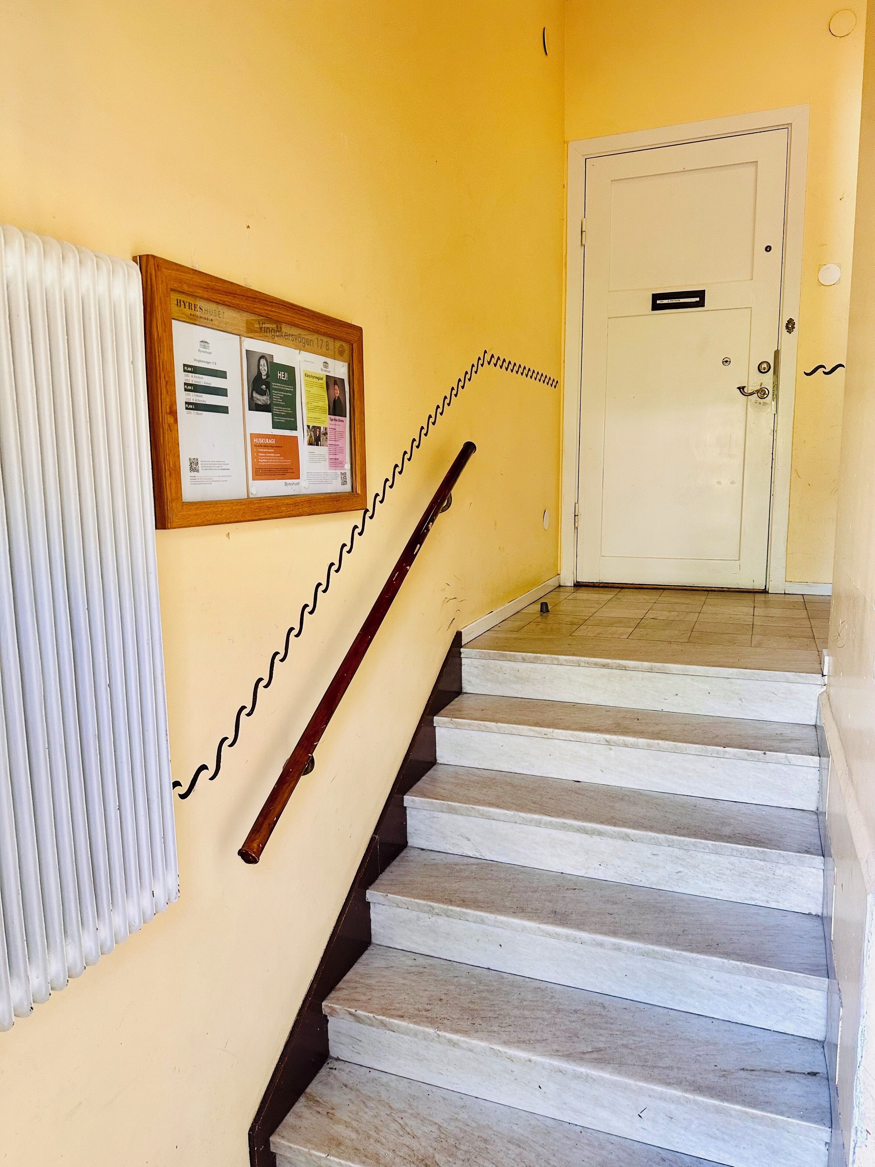A staircase with a handrail, a bulletin board with notices, and a door at the top.