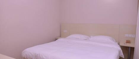 Une chambre d’hôtel standard, avec un lit simple, une table de chevet et un petit bureau.