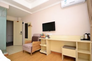 A hotel room with a bed, a desk, a chair, a television, and an air conditioning unit.