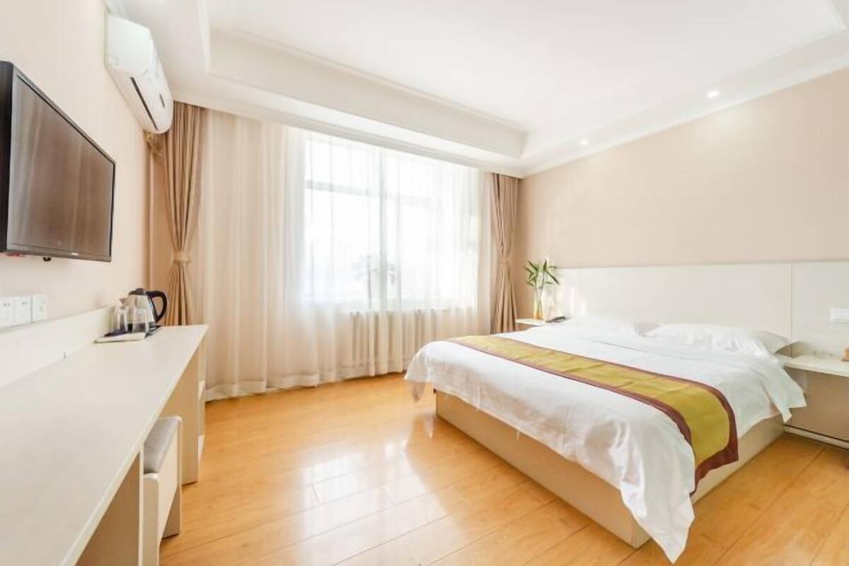 A hotel room with a bed, a desk, a television, and a window with curtains.